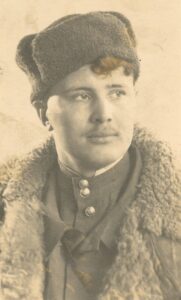Zdjęcie portretowe młodego radzieckiego żołnierza. Ubrany jest w gimnastjorkę i jasny kożuch Na guzikach bluzy mundurowej widać pięcioramienne gwiazdy. Na głowie ma czapkę uszankę spod której wystają, krótkie, falujące włosy. Ma pogodną twarz. Wzrok skierowany w lewe stronę.