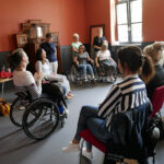 Cztery kobiety na wózku inwalidzkim, obok nich trzy uśmiechnięte kobiety. Zdjęcie przedstawia szkolenie w ramach programu "Kultura dostępna" dotyczące potrzeb osób z niepełnosprawnością ruchu.
