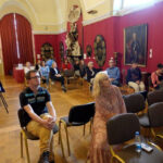 Salę wypełnia zgromadzona widownia siedząca na krzesłach. Publiczność słucha kobiety. Zdjęcie przedstawia szkolenie dla pracowników muzeum "Dostępność dla osób ze spektrum autyzmu".